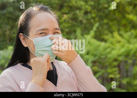 Seitenansicht Porträt der glücklichen asiatischen Frau auf schützende Gesichtsmaske im Freien. Kopierbereich. Gesundes Konzept. Stockfoto