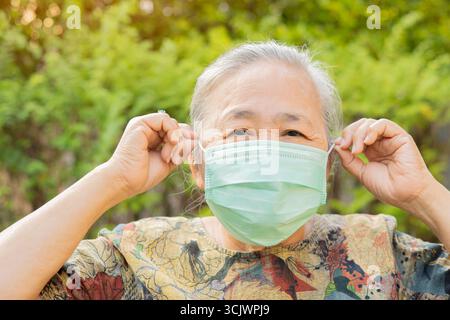 Asiatisches Seniorporträt und Nahaufnahme mit Medizinmaske auf dem Gesicht über Naturhintergrund. Senior Healthy Konzept. Stockfoto