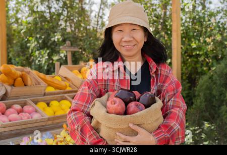 Eine junge Landwirtin, die über ihrem ländlichen Obstkiosk steht und frische rote Äpfel hält, die im Garten selbst geerntet wurden. Stockfoto