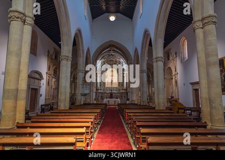 Das große Innere der Kirche St. Johannes des Täufers in Tomar, mit einem langen roten Teppich, der zu einem reich verzierten vergoldeten Altar führt, flankiert von hohen bogenförmigen Ko Stockfoto