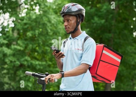 Schwarzer Mann, Der Mit Dem Fahrrad Unterwegs Ist Und Lebensmittel Mit Dem Smartphone Liefert Stockfoto