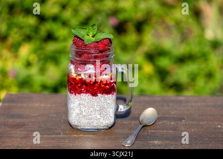 Gesunder Chia-Pudding im Glasbecher mit frischer roter Himbeere, Chiasamen, Marmelade, Walnüssen, Kokosmilch und Honig zum Frühstück auf einem Holztisch auf Natu Stockfoto