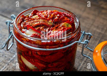 Sonnengetrocknete rote Tomaten mit Knoblauch, Olivenöl und Gewürzen in einem Glas auf einem Holztisch. Rustikaler Stil, Nahaufnahme Stockfoto