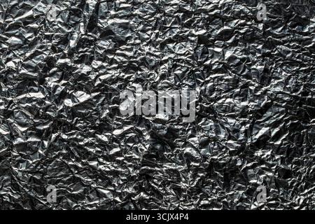 Hintergrund und Textur der gebrauchten zerknitterten Schokoladenfolie, Nahaufnahme, Draufsicht. Glänzende Aluminiumfolie ohne Schokoladenbonbons Stockfoto