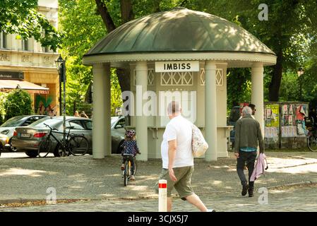 Eine offene Straßenszene von einem sonnigen Tag im historischen Stadtteil Rixdorf in Berlin. In der Mitte befindet sich ein klassischer „Imbiss“ (Imbiss) mit Kuppeln. Stockfoto