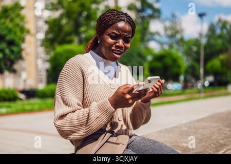 Afroamerikanerin ist besorgt, wenn sie ihr Smartphone für Online-Nachrichten nutzt. Stockfoto