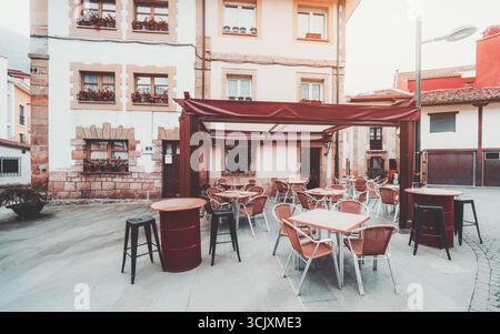 Gemütliche, leere Außenterrasse auf einem bezaubernden europäischen Stadtplatz mit roten Tischen, Korbsesseln und klassischer Architektur mit Blumen Stockfoto
