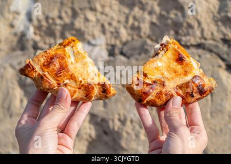 Zwei Scheiben maltesischer Pizza halten in den Händen der Frau mit Steinhintergrund, Gozo, Malta Stockfoto