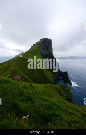 Eine atemberaubende Klippe erhebt sich dramatisch aus dem Meer, umgeben von üppigem grünem Gras auf den Färöern. Kallur Lighthouse, Kalsoy Island Stockfoto