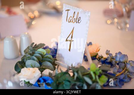 Eleganter Tisch für einen Hochzeitsempfang, mit einem Blumenarrangement aus Hortensien, Rosen und Eukalyptus, das den Tisch Nummer 4 umgibt Stockfoto