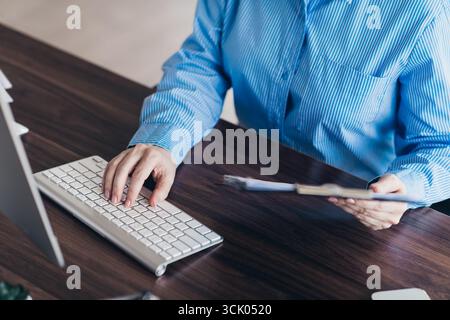Professionelle Frau, die an einem Computer in einer modernen Büroumgebung arbeitet und Aufgaben mit Dokumenten und Technologie bearbeitet Stockfoto