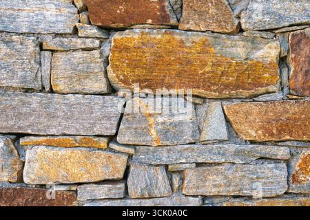 Nahaufnahme einer alten Steinmauer aus natürlichen braunen und grauen Felsen in einem rustikalen Mauerwerk, mit rauer Oberflächenstruktur und traditionellem Co Stockfoto
