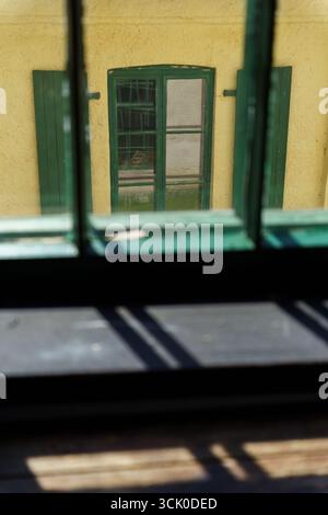 Sonnenlicht durch das Fenster mit Holzfenster in einem alten gelben Betongebäude auf der gegenüberliegenden Seite Stockfoto