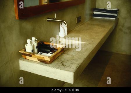 Ein industrieller Kosmetikbereich mit Betonarbeitsfläche, Wandarmatur, Toilettenartikeln und Handtüchern Stockfoto