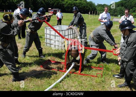 Feuerwehrleute in alten Uniformen, die eine manuelle Sprinklerpumpe mit Wassertank während einer historischen Brandbekämpfungsdemonstration in Rudawka Rymanowska, Podk, betreiben Stockfoto