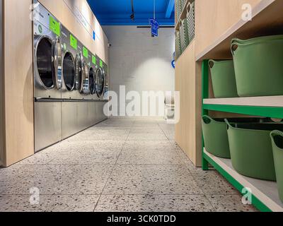 Riga, Lettland - 04. September 2025: Zeitgenössischer Waschraum mit Speed Queen Waschmaschinen und grünen Körben in einer Selbstbedienungs-Münzwaschanlage Stockfoto