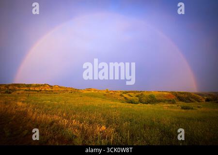 Ein atemberaubendes Bild fängt die lebendigen Farben eines wunderschönen Sonnenuntergangs ein, der den Himmel malte, mit einem herrlichen Regenbogenbogen über weite, offene Wiesen Stockfoto