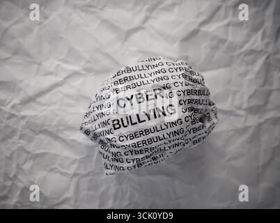 Zerknitterte Papierkugel mit Worten Cyberbullying auf zerknittertem weißem Papierhintergrund. Stockfoto