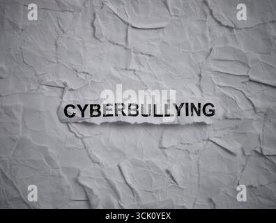 Zerknittertes Stück Papier mit Wort Cyberbullying auf einem zerrissenen zerknitterten weißen Papierstückchen Hintergrund. Stockfoto