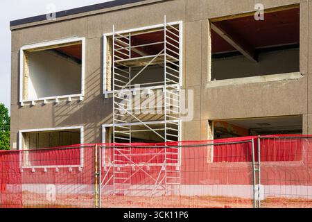 Außenbereich des Gebäudes, das renoviert wird, mit Gerüsten und rotem Sicherheitszaun, mit Fensterwechsel und Baustellenvorbereitung Stockfoto