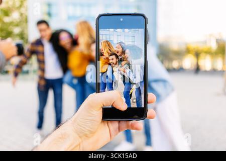 Hand hält das Smartphone, um Fotos von verspielten Freunden in der Stadt zu machen Stockfoto