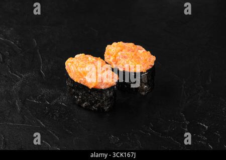 Scharfes Gunkan Maki Sushi mit gehacktem Lachs und Tobiko auf schwarzem Hintergrund Stockfoto