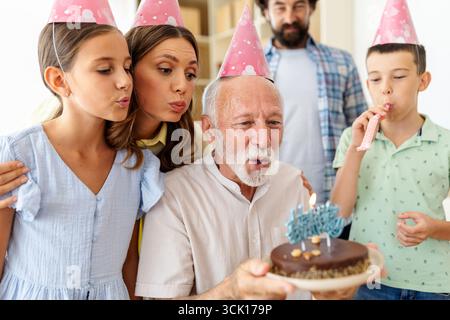 Eine fröhliche Geburtstagsfeier findet statt, wenn Familienmitglieder einen Großvater umgeben. Sie blasen Kerzen aus und genießen den besonderen Moment zusammen. Stockfoto