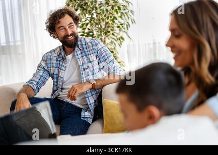 Der Mann genießt zwangloses Gespräch mit Frau und Kind im hellen Wohnzimmer und fördert die Verbindung und das Lachen während des gemütlichen Nachmittags Stockfoto