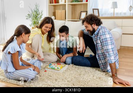 Eine vierköpfige Familie versammelt sich in ihrem Wohnzimmer für einen lustigen Spielabend, um gemeinsam auf einem weichen Teppich zu lachen und gute Zeiten zu genießen Stockfoto