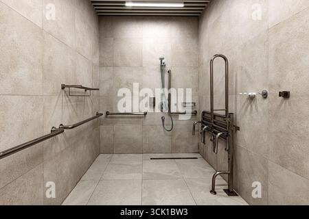 Innenansicht einer modernen, barrierefreien Dusche mit Sicherheitsgriffen aus Edelstahl, einer Klappbank und verstellbarem Duschkopf. Der gekachelte Raum o Stockfoto