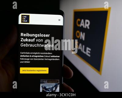 In dieser Fotoabbildung hält eine Person ein Handy mit der Webseite des deutschen Unternehmens CarOnSale (Castle Tech GmbH) vor dem Logo. Stockfoto
