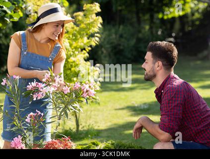 Junge Frau, die sich um Blumen im Garten kümmert, mit Mann, der sich in der Nähe hockt und ihre Arbeit bewundert Stockfoto