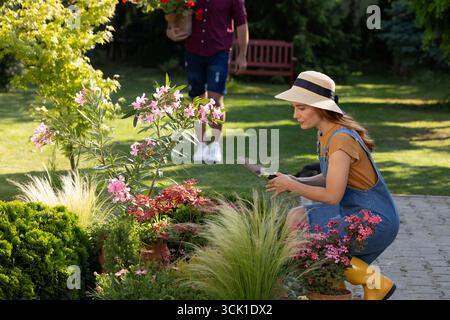 Leute arbeiten fleißig im Garten. Zugeschnittenes Bild mit Fokus auf Frau, die sich neben Blumen hockt und Kelle verwendet Stockfoto