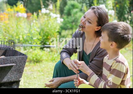 Kaukasische Frau, die Würstchen auf einem Grill mit ihrem Sohn grillt. Stockfoto
