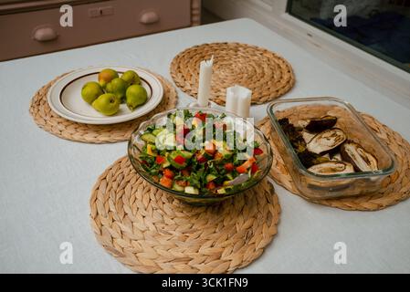Ein gesundes und köstliches Mittagessen ist wunderschön auf einem Esstisch angeordnet, mit einem lebhaften gemischten Salat, gerösteten Auberginen, frischen Birnen und Kerzen, die eine gemütliche und einladende Atmosphäre schaffen Stockfoto