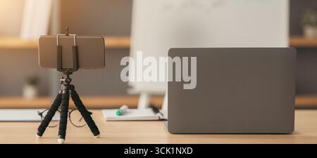 Arbeitsplatz des Tutors, des Lehrers während der covid Pandemie. Laptop, Notizblöcke, Smartphone auf Stativ, Wasser auf Tisch Stockfoto