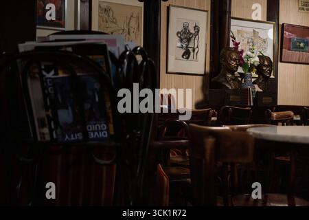 Werfen Sie einen Blick durch Zeitschriften in ein historisches gemütliches Café in Wien mit beigefarbenen Streifentapeten, mehreren gerahmten Gemälden und zahlreichen kleinen Tischen. Stockfoto