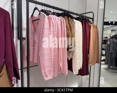 Farbenfrohe Strickwaren und Cardigans auf Kleiderbügeln sind ordentlich in einem Modeeinzelhandel angeordnet. Einkaufsmöglichkeiten, saisonaler Stil, Textilhandel und Stockfoto
