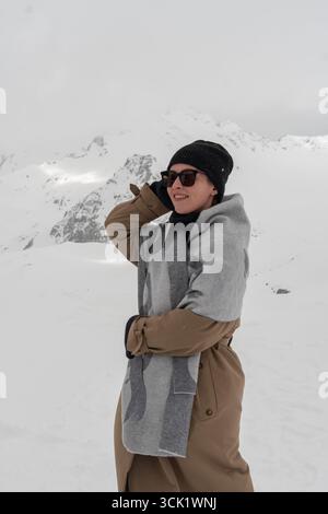 Eine Frau lächelt warm im kalten Wind, während sie in einem schneebedeckten Bergtal steht Stockfoto