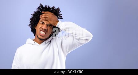 Afroamerikanischer Teenager, der unter Kopfschmerzen leidet und seine Stirn über violettem Studiohintergrund berührt Stockfoto