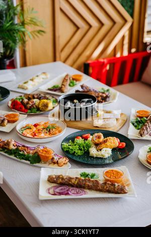 Blick von oben auf verschiedene gegrillte Fleischgerichte, Meeresfrüchte und Beilagen an einem Restauranttisch Stockfoto