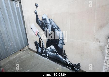 London, Großbritannien. 9. September 2025. Ein neues Werk des weltberühmten, anonymen Straßenkünstlers BANKSY erschien gestern vor den königlichen Justizgerichten, in dem ein Richter seinen Hammer auf einen niedergeschlagenen Demonstranten mit einem Plakat bringt. Es folgte auf die Verhaftung von 857 friedlichen Demonstranten auf dem Parlamentsplatz, die Plakate zur Unterstützung der Palästinensischen Aktion hielten. Verborgen von einem Metallschutzschirm war das Kunstwerk heute durch eine kleine Lücke sichtbar, und die Leute standen in der Warteschlange, um einen Blick zu erhalten. Derzeit ist unklar, was mit dem Graffiti geschehen wird. Quelle: Ron Fassbender/Alamy Live News Stockfoto