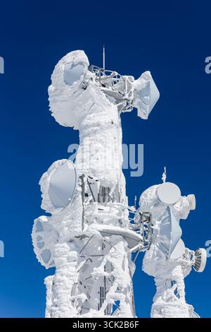 Eisiger Telekommunikationsmast auf einem Berggipfel vor einem klaren blauen Winterhimmel Stockfoto