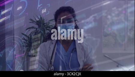 Stehende Ärztin faltet Arme mit Maske und Stethoskop in der Klinik, mit digitalen Overlays Stockfoto