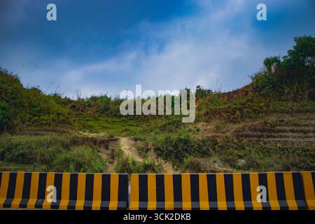 Ein landschaftlich schöner Hügel mit grüner Vegetation und einem dramatischen, bewölkten blauen Himmel darüber, der eine ruhige und natürliche Landschaft im Freien in Chattogram, Bang, schafft Stockfoto