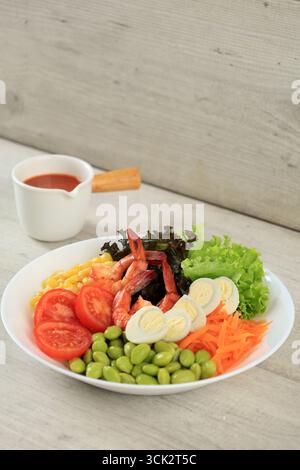 Frischer hausgemachter Garnelensalat mit Edamame, Wachteleier, Tomaten, Karotten, Mais, und Salat auf weißer Platte, serviert mit süßer und scharfer Sauce. Stockfoto