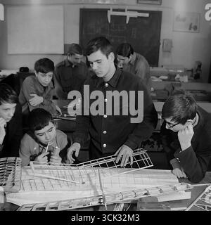 Ein archiviertes Schwarzweißfoto, aufgenommen im Februar 1975 in Sloviansk, ukrainische SSR, das eine Sitzung eines Flugzeugmodellierclubs im Haus der jungen Techniker oder einer Berufsschule (PTU) aufnimmt. Ein junger Mentor zeigt einer Gruppe enthusiastischer Teenager den Entwurf eines Flügels für ein großes Modellflugzeug auf Blaupausen. Diese Szene ist ein Paradebeispiel für das sowjetische System der außerschulischen technischen Ausbildung, das darauf abzielt, zukünftige Ingenieure und Piloten zu fördern, und vermittelt eine Atmosphäre der kreativen Arbeit und der Jugendlichen Träume vom Himmel Stockfoto