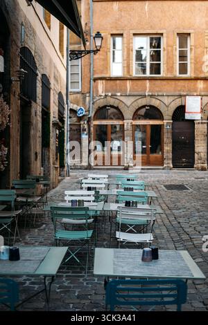 Leeres Café im Freien mit pastellfarbenen Metallstühlen und Tischen in einer kopfsteingepflasterten Straße vor historischen ockerfarbenen Gebäuden. Europäischer Lebensstil, urbane Ruhe Stockfoto