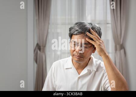 Ein älterer asiatischer Mann leidet zu Hause an Kopfschmerzen. Stockfoto