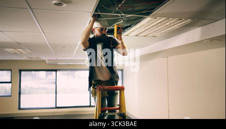 Elektriker, Decke und Mann im Büro mit Draht, Test oder Sicherheit zur Qualitätskontrolle. Inspektion, Wartung und Techniker am Arbeitsplatz mit Multimeter Stockfoto